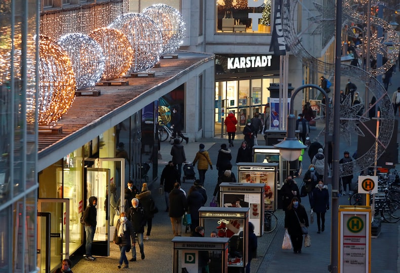 People with protective face masks walk beside Christmas themed lights at Schloss Strasse shopping street in Berlin