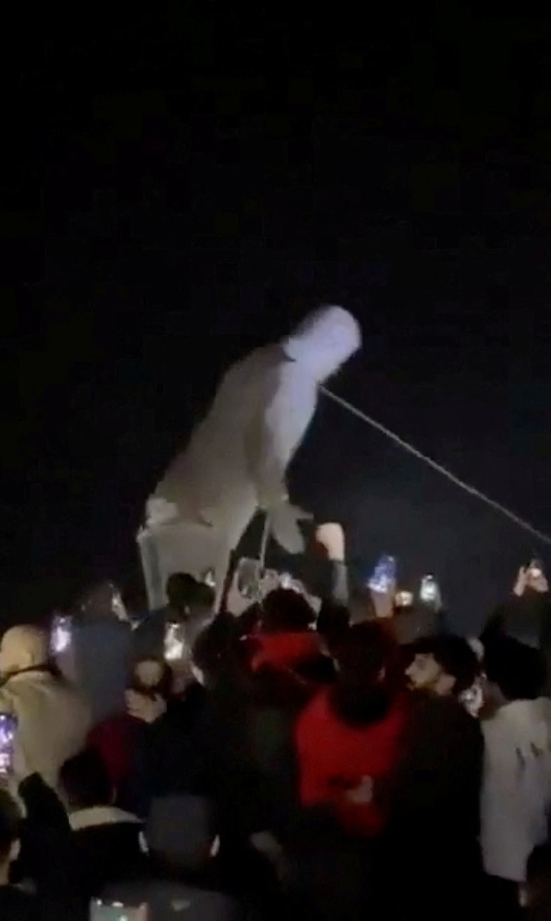 La gente aplaude cuando se derriba la estatua del ex presidente de Siria, Hafez al-Assad, en Homs.